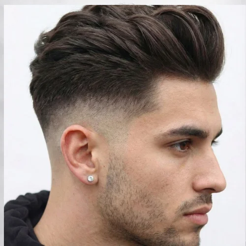 Side profile of a man with a low fade—skin-faded around the ear and neckline—and a longer, textured French crop on top styled into a voluminous, brushed-up fringe.